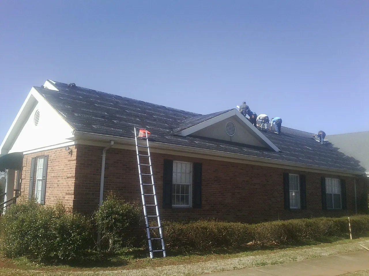 Crew tearing shingles off a brick ranch roof with a ladder set — Emergency Roof Repair work by our crew in Belgium