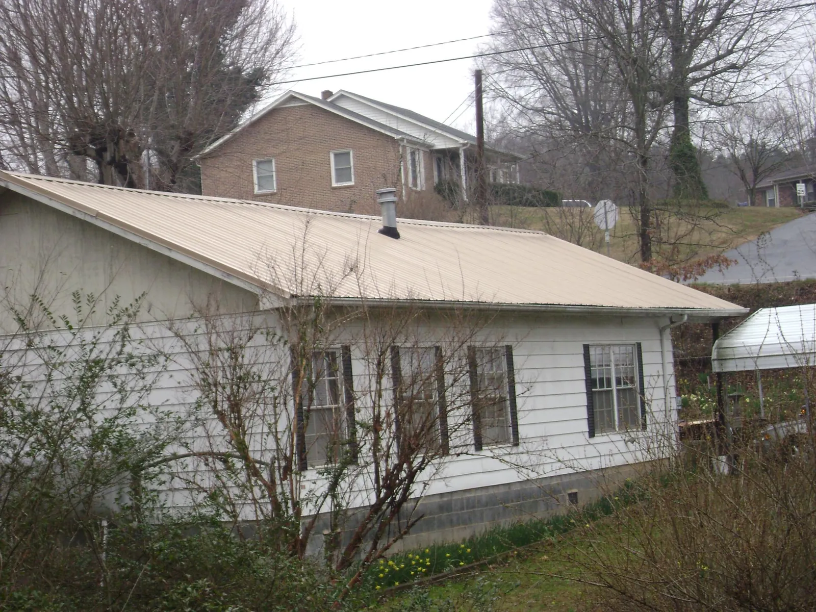Tan metal roof on a white sided house set into a hillside — Commercial Roofing by Roofing Brothers in Belgium