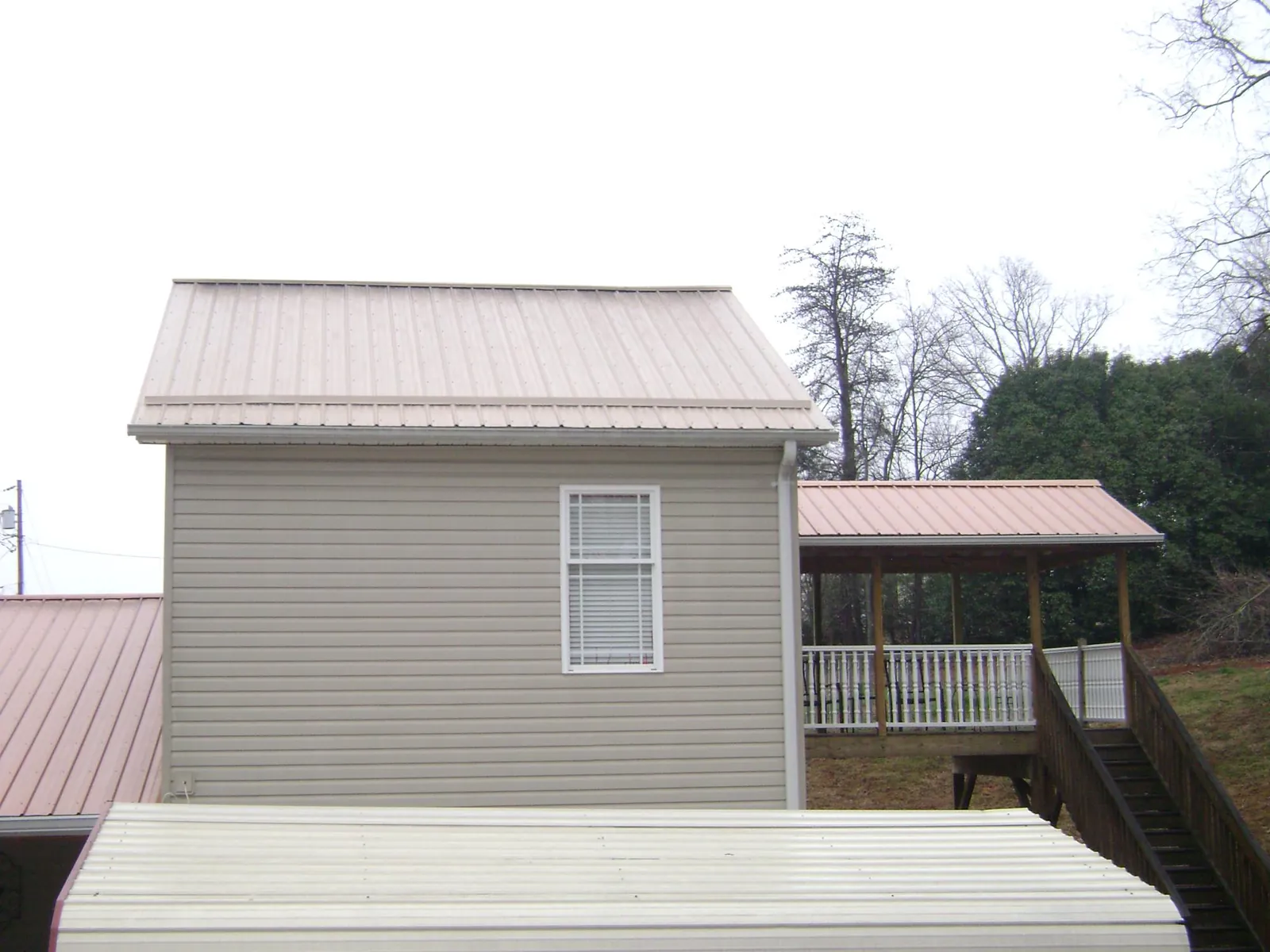 Tan metal roofs on a two story addition and attached porch, from a Roof Replacement job in Belgium